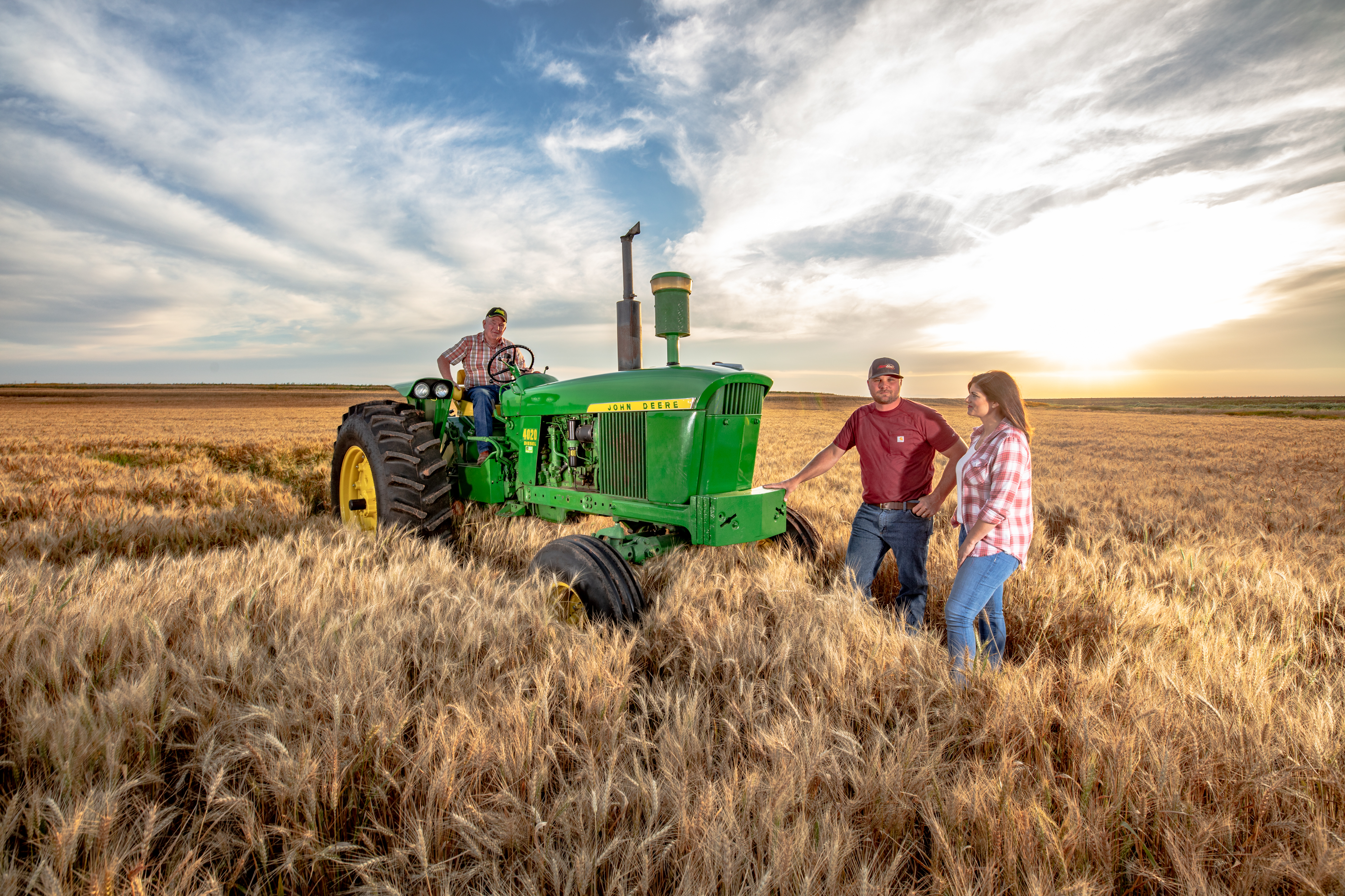 the hunt family poses in their fields at sunset with their tractor